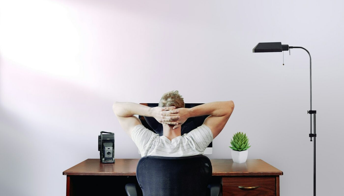 man holding his head while sitting on chair near computer desk